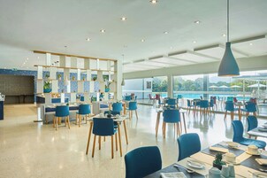 A spacious dining area with blue chairs and tables, a kitchen area with a counter, and large windows offering a view of the outdoors.