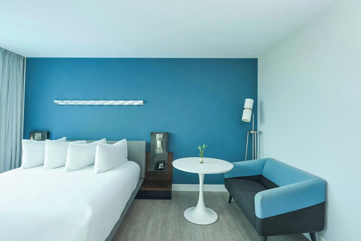 A hotel room with a bed, a small round table, a sofa, and a blue accent wall.