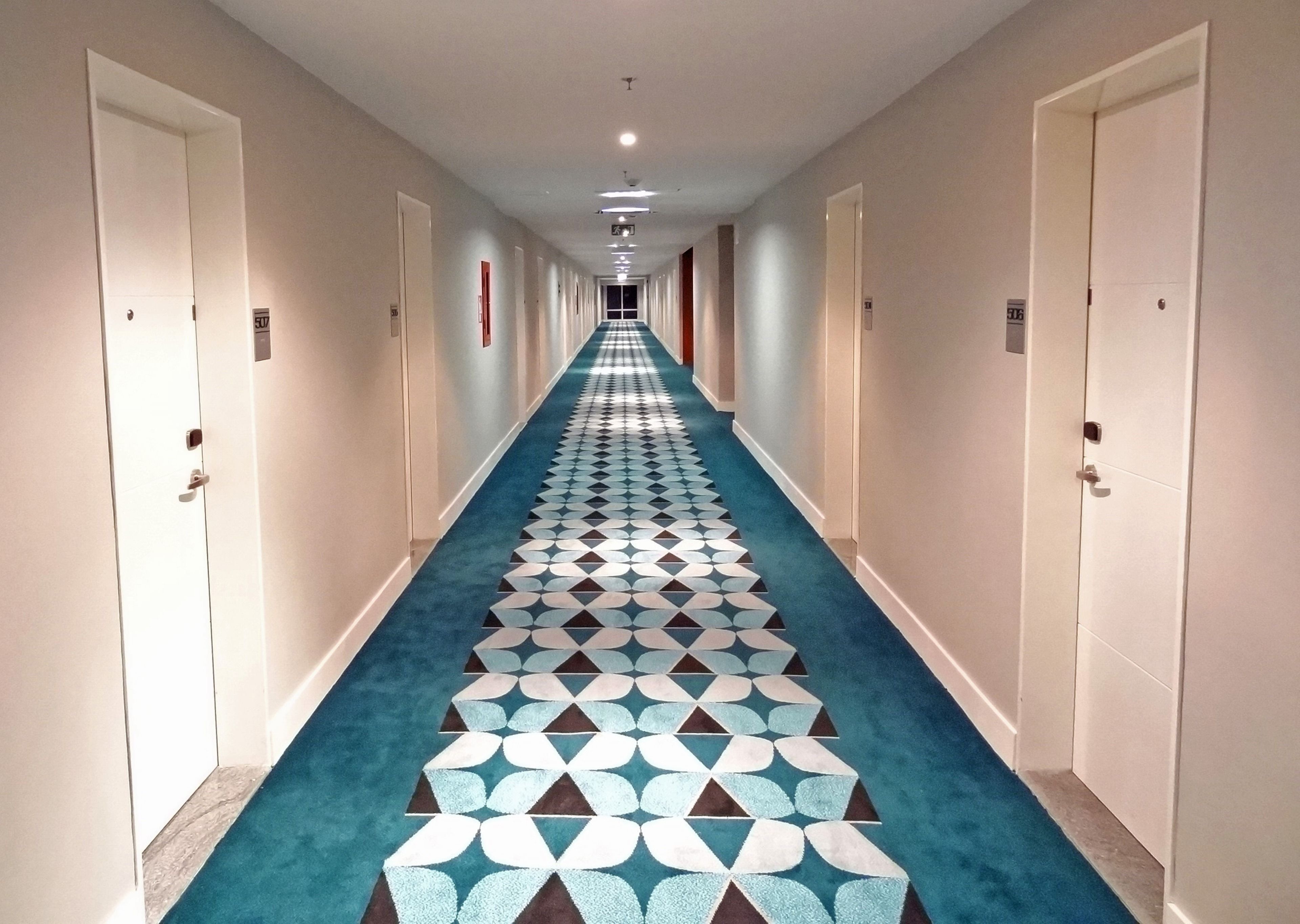 A hotel hallway with a patterned carpet, doors on both sides, and a ceiling light.