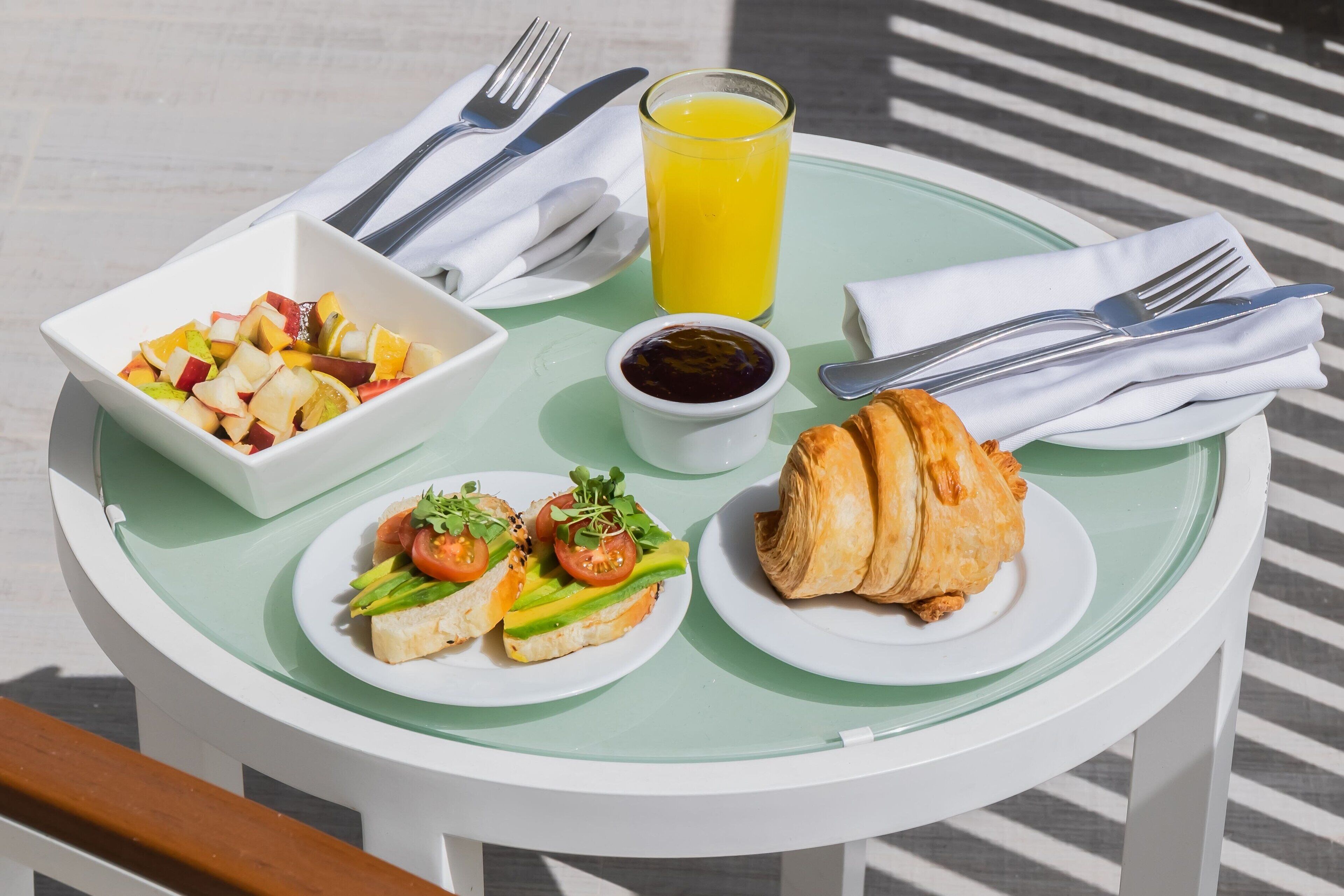 Ett frukostbord med en fruktsallad, ett glas apelsinjuice, en croissant och en liten skål med sylt.