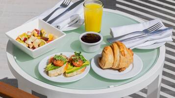 Ett frukostbord med en fruktsallad, ett glas apelsinjuice, en croissant och en liten skål med sylt.