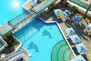 An aerial view of a swimming pool with dolphin murals, surrounded by umbrellas and palm trees. - Marriott Maracay Golf Resort (Maracay)