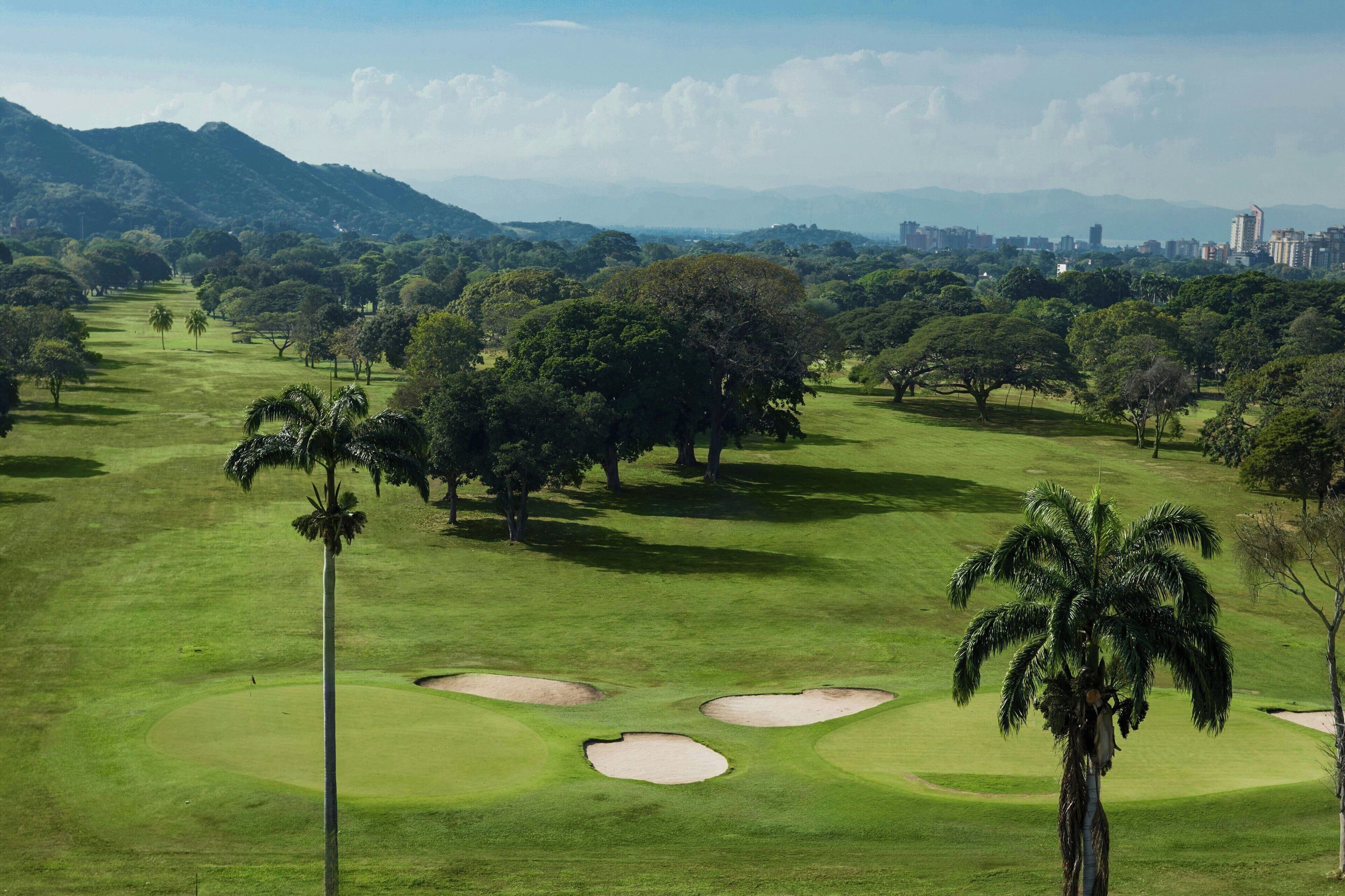 A golf course with multiple sand bunkers, palm trees, and a distant city skyline.