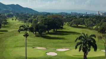 A golf course with multiple sand bunkers, palm trees, and a distant city skyline.