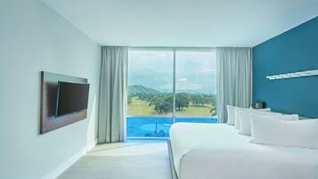 Habitación de hotel con una cama grande, un televisor de pantalla plana montado en la pared y vistas a un campo de golf y montañas a través de la ventana.