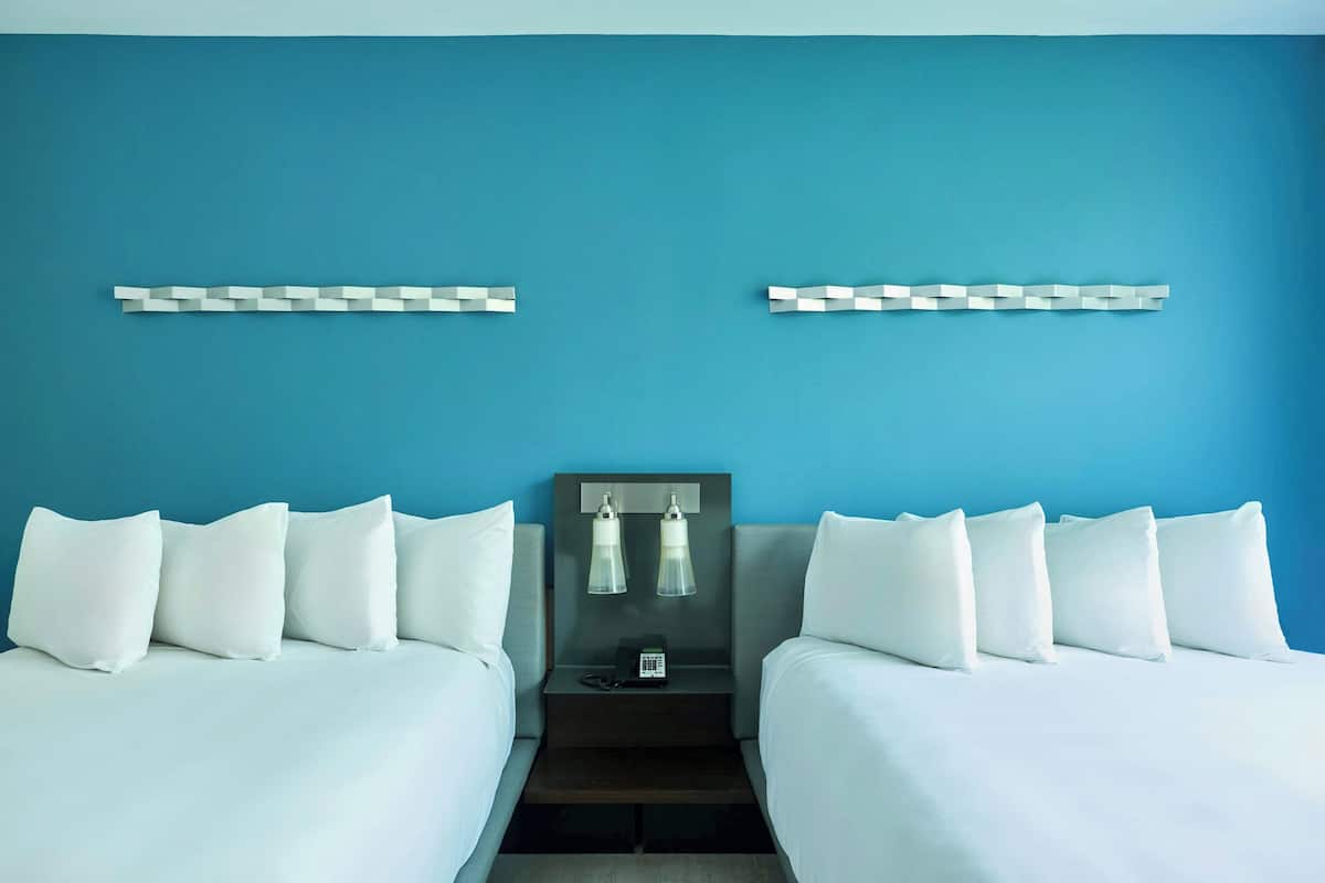 A hotel room with two beds, a nightstand, and a wall-mounted lamp.