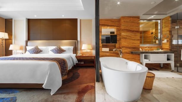 A modern hotel room with a large bed, a separate bathroom with a freestanding bathtub, and a large mirror. - Juva Grand Hotel (Hohhot)