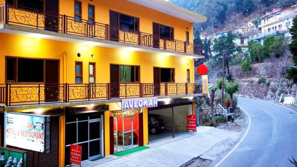 Un hotel de dos plantas con balcones, un letrero que dice 'Avlokan Hotel & Restaurant', y vistas de un paisaje montañoso.