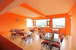 A dining area with tables and chairs, large windows, and a view of the outdoors. - Hotel Avlokan (Nainital)