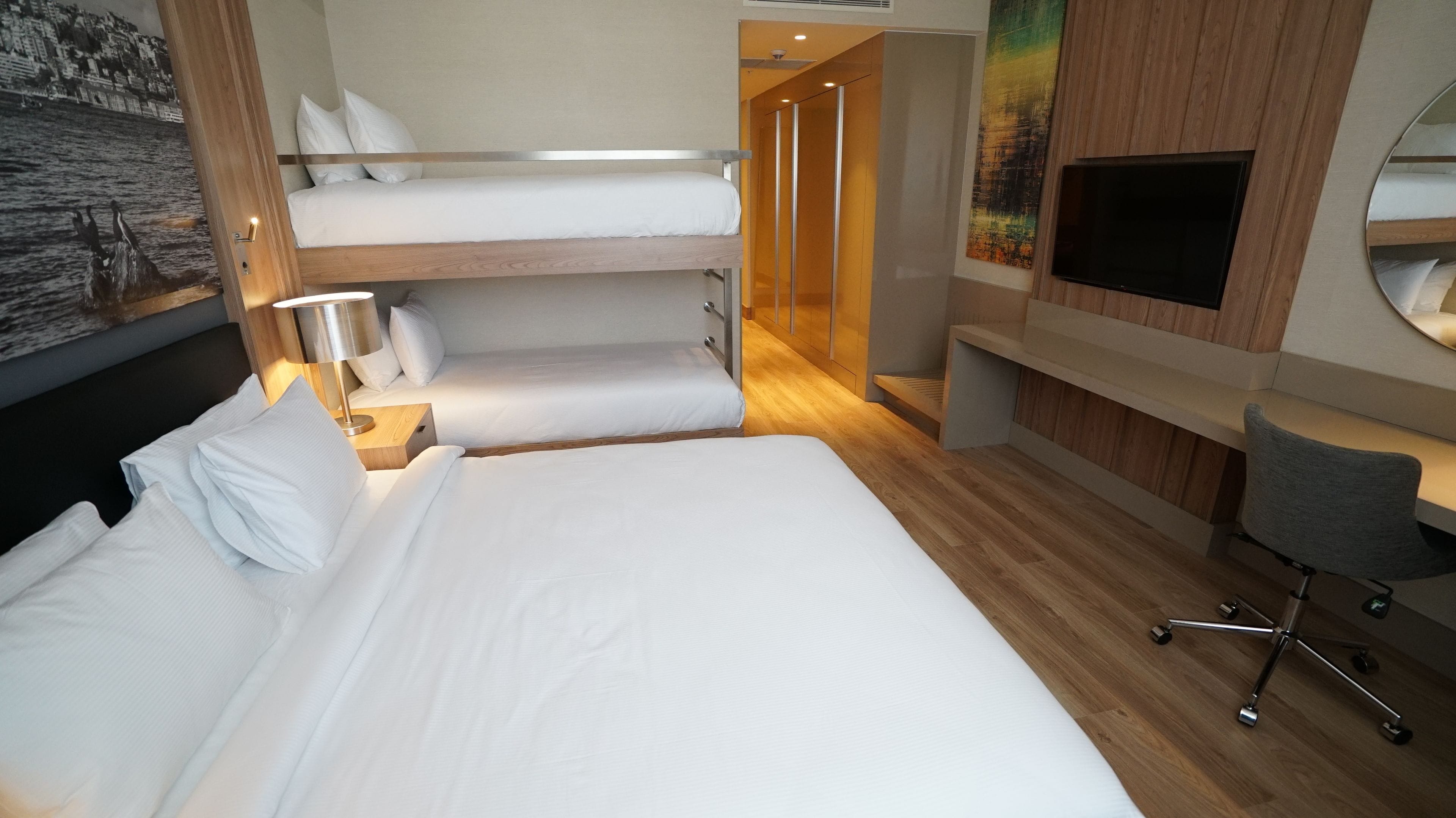 A hotel room with a large bed, a desk with a chair, a TV, and a painting on the wall.