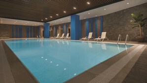 Una piscina interior con agua cristalina, rodeada de sillones de descanso y un diseño de techo moderno.