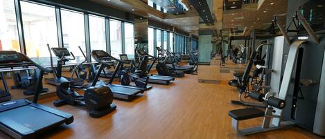 Une salle de sport équipée de plusieurs tapis de course, de plusieurs appareils de musculation elliptiques et de matériel de musculation.