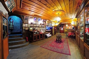 Staircase leads to an upper level, flanked by shelves and framed pictures, with a traditional table and chairs below.