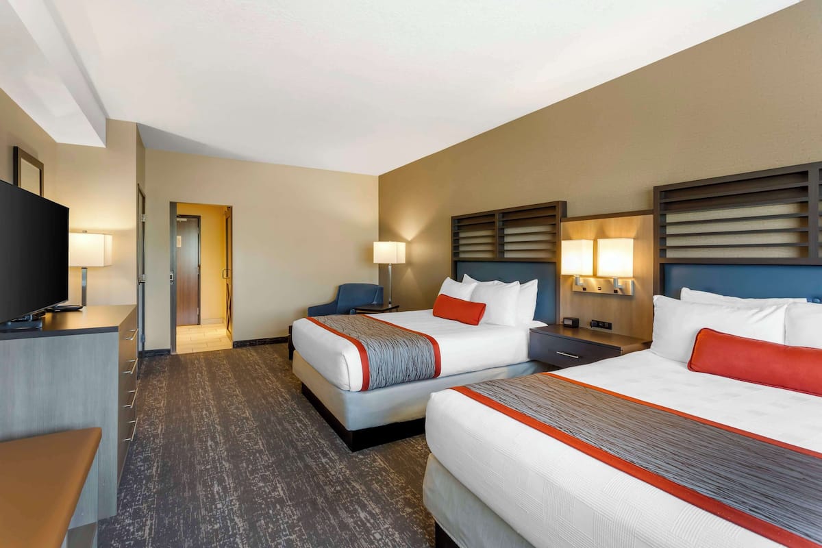 A hotel room with two beds, a desk, a TV, and a chair.