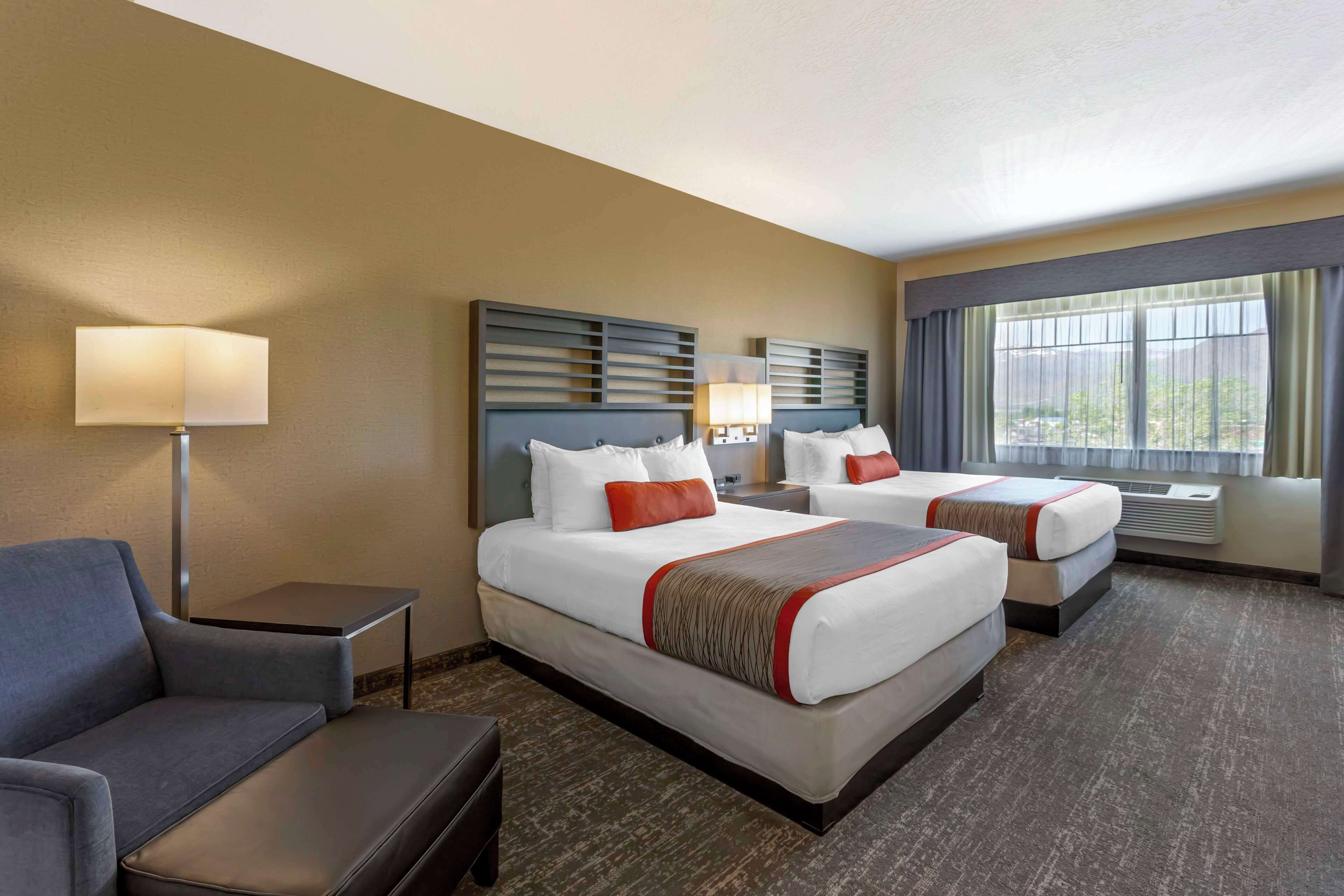 A hotel room with two beds, a sofa, a desk, and a lamp.