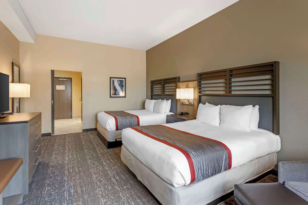 A hotel room with two beds, a desk, a TV, and a door leading to a bathroom.