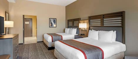 A hotel room with two beds, a desk, a TV, and a door leading to a bathroom.
