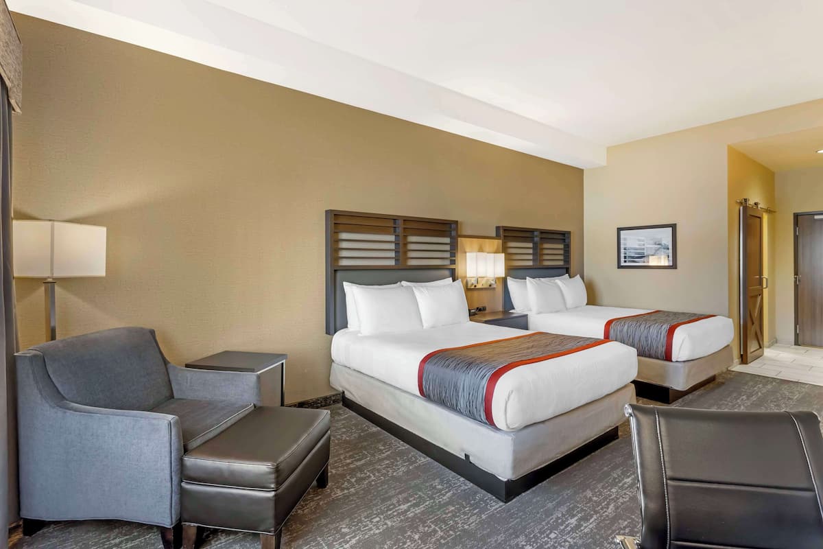 A hotel room with two beds, a sofa, a desk, and a lamp.