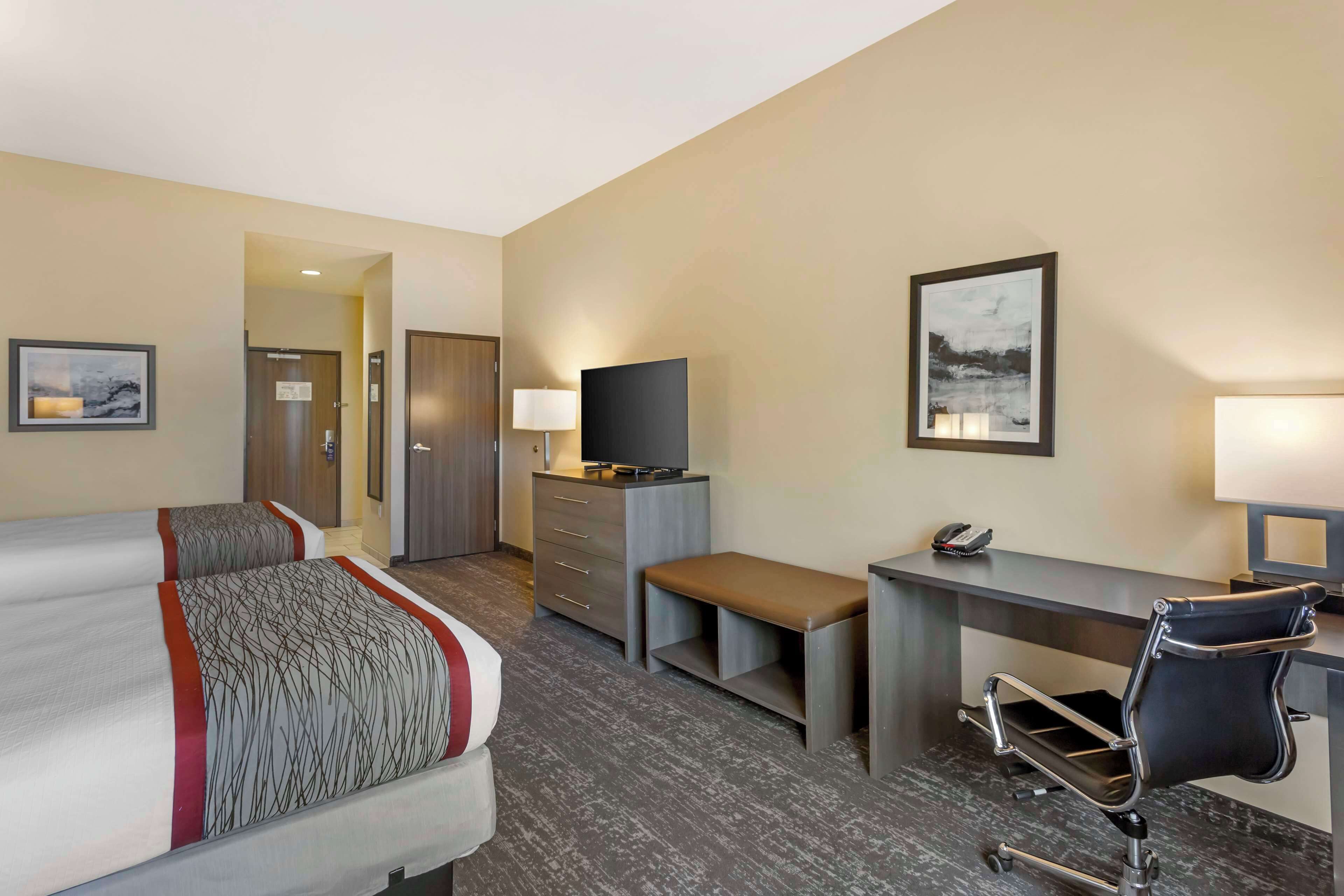 Una habitación de hotel con dos camas, un escritorio, una silla, un televisor y una lámpara de escritorio.