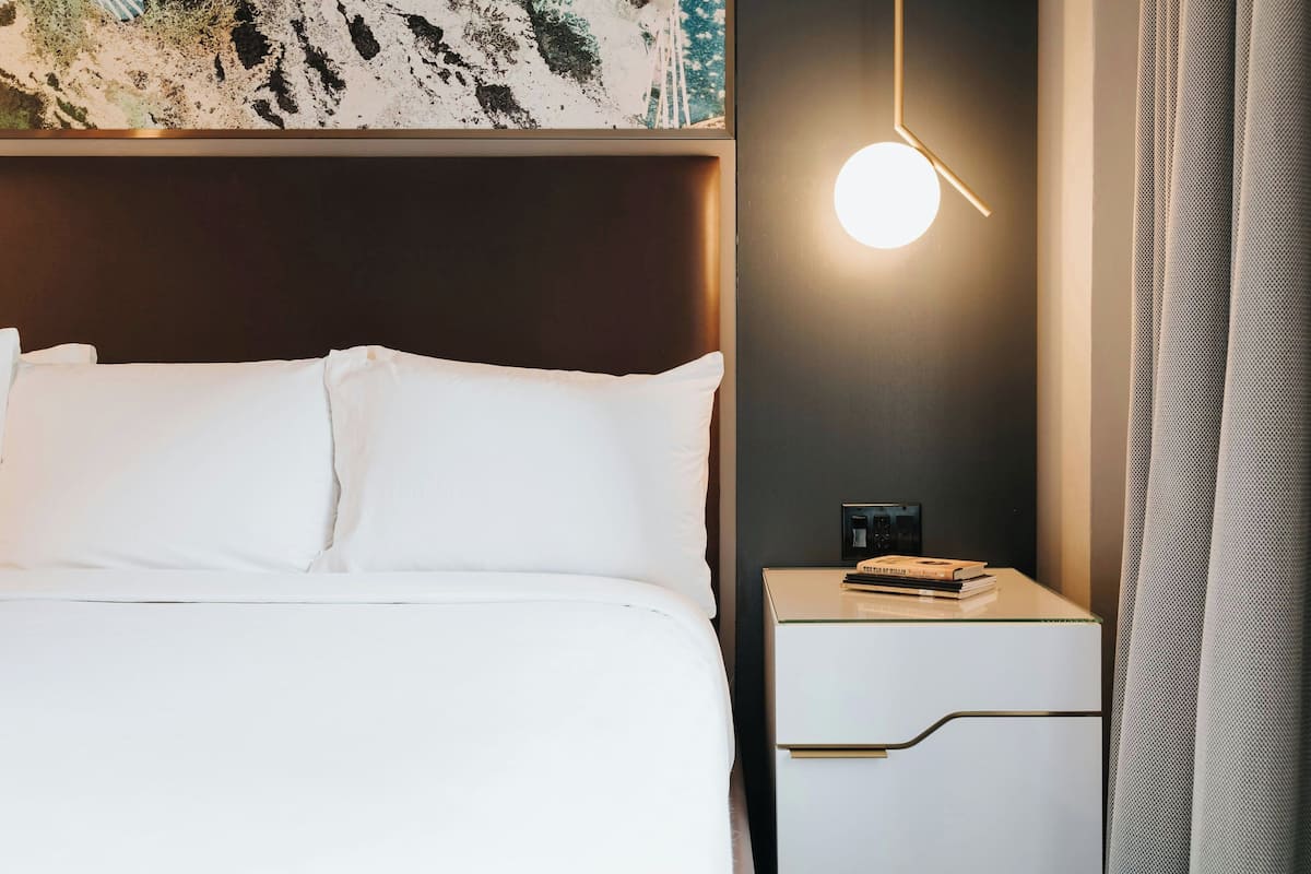 A neatly made bed with white linens, a bedside table with a lamp, and a wall-mounted artwork above the bed.