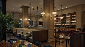Een restaurant met hoge plafonds, hangende verlichting en een bar met flessenkasten.