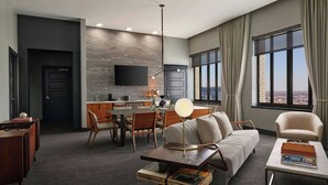 Een moderne hotelkamer met een zithoek, eethoek en een groot raam met uitzicht op de stad.