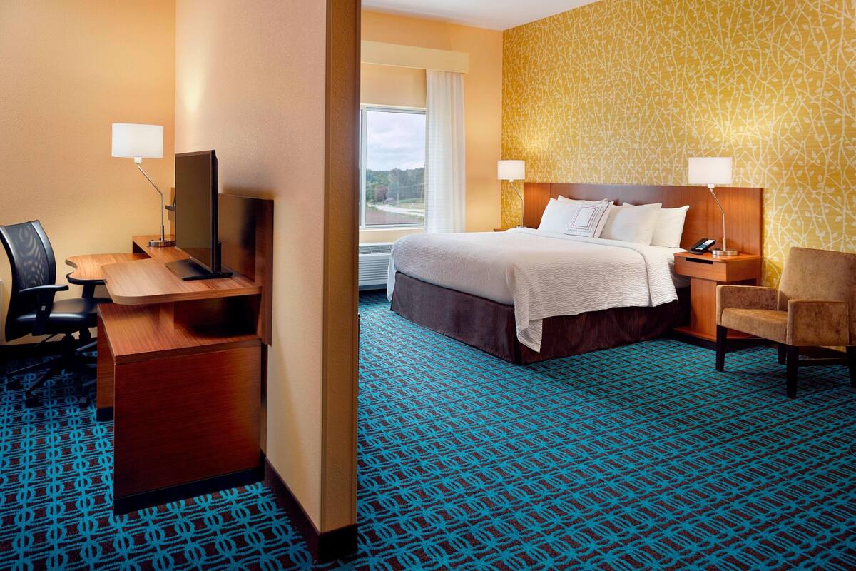 A hotel room with a bed, desk, chair, and a large window.