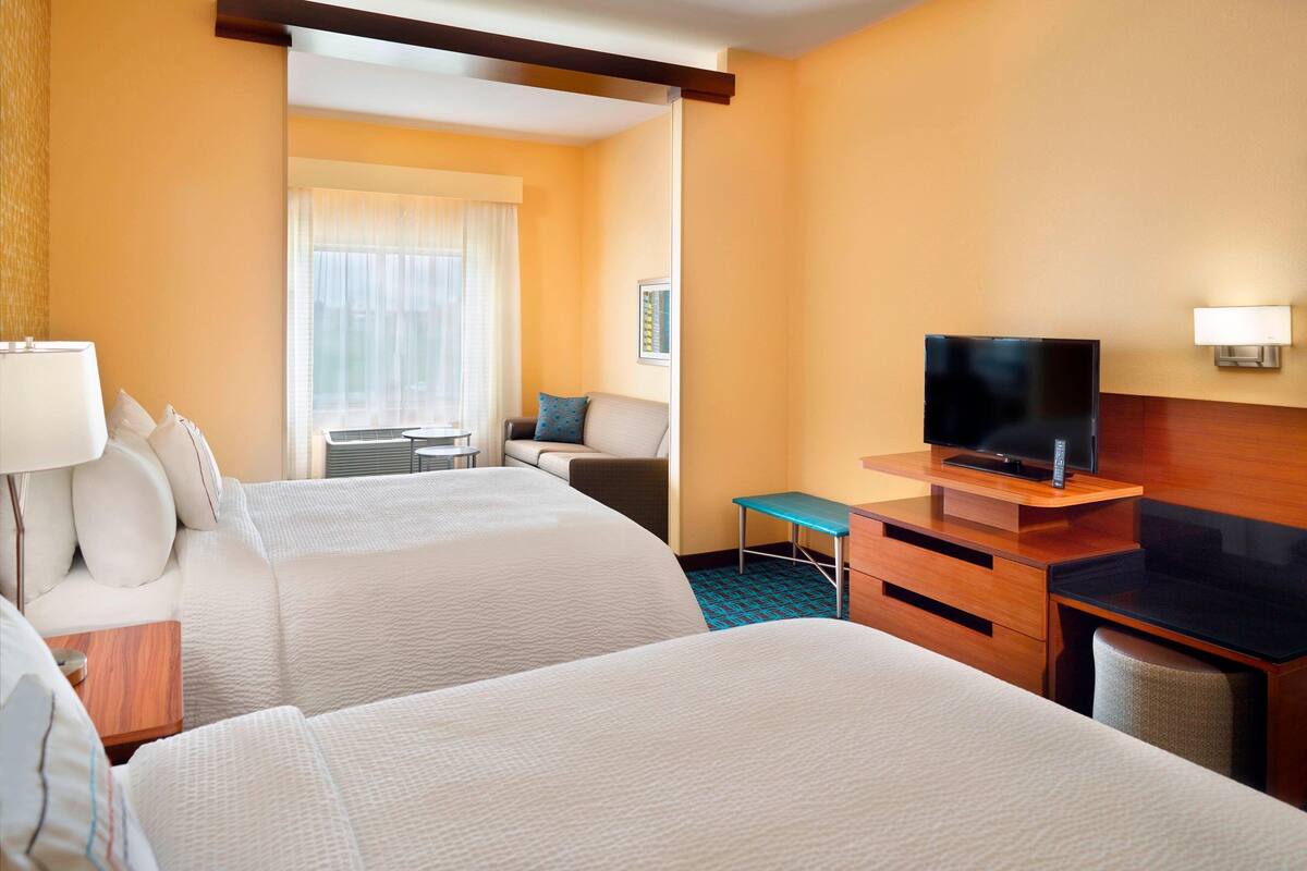 A hotel room with two beds, a desk, a TV, and a window with curtains.