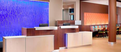 A hotel reception area with a modern design, featuring a reception desk, a large illuminated wall, and a seating area with chairs and tables.