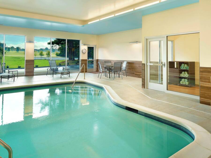 Una piscina interior amb vistes a un camp de golf, envoltada de gandules i una zona de seients amb una taula.
