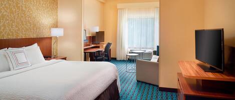 Habitación de hotel con una cama grande, un escritorio con computadora, un televisor y vistas al exterior.