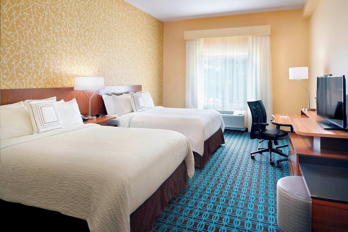 A hotel room with two beds, a desk with a computer, a TV, and a window with curtains.