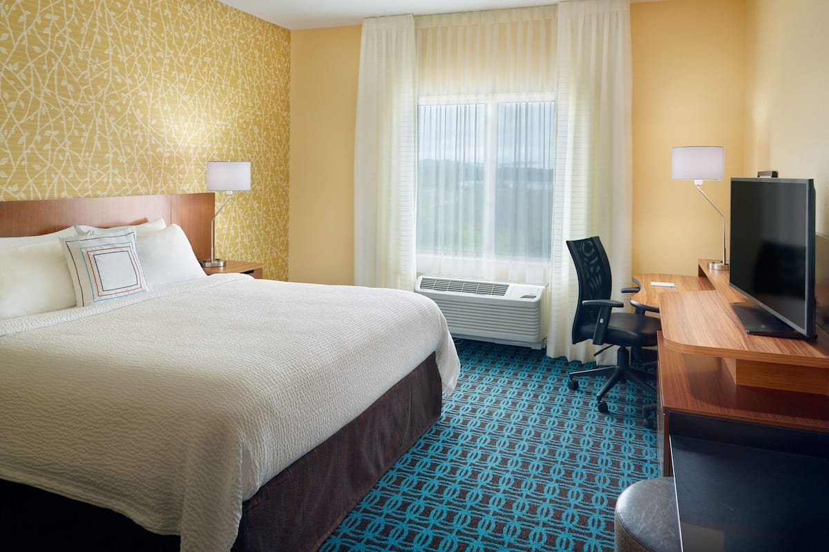 A hotel room with a large bed, a desk with a television, a chair, and a window with curtains.