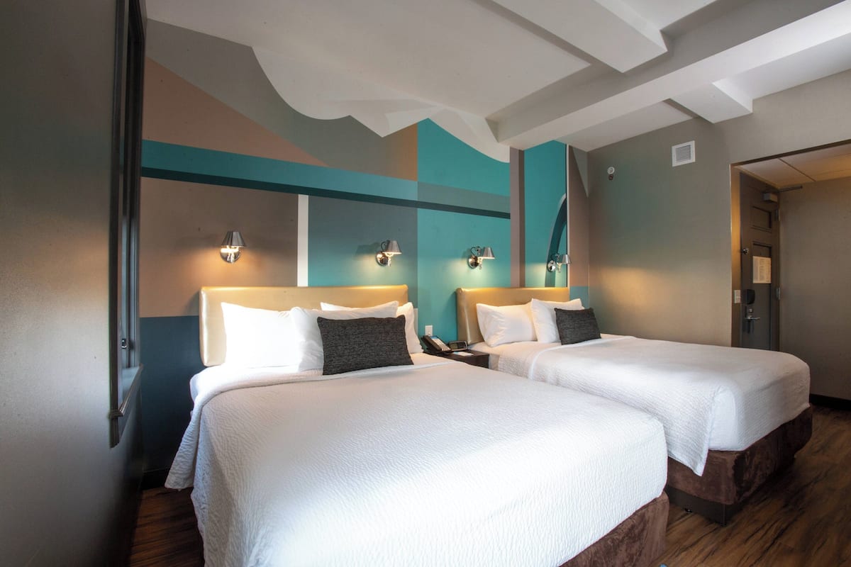 Ein Hotelzimmer mit zwei Betten, jeweils mit Kopfteil, Nachttischen und Lampen.