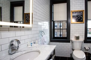Un baño moderno con azulejos blancos tipo metro, un lavamanos de mármol, un grifo cromado, un inodoro y una ventana con vistas a edificios.