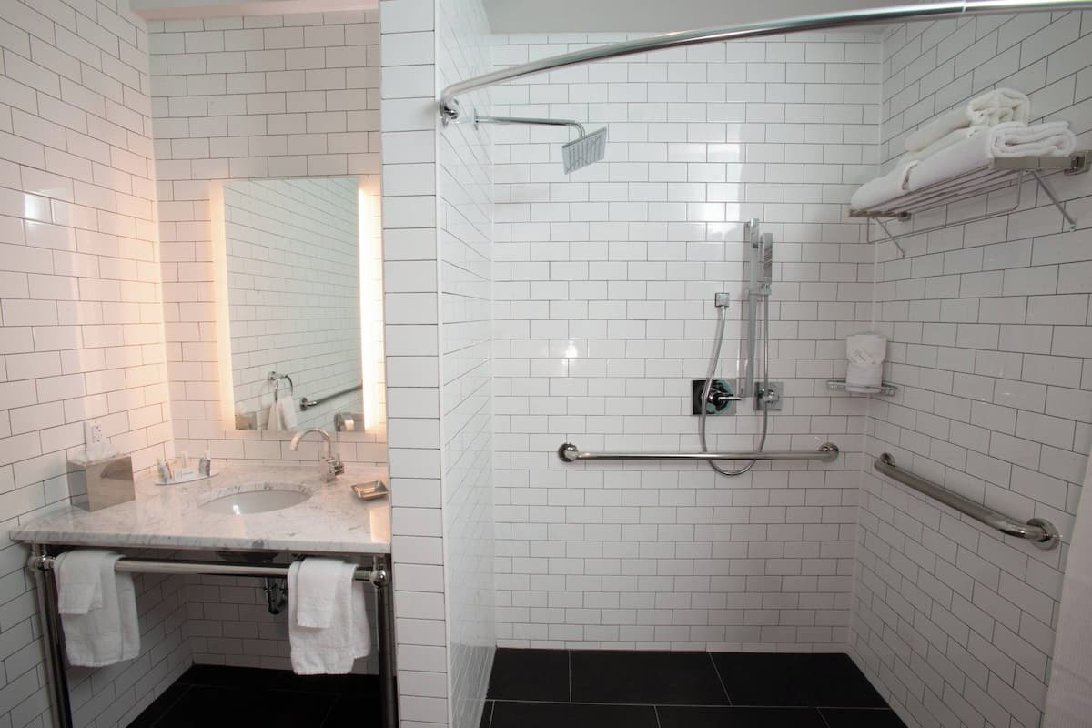 Ein modernes Badezimmer mit weißen Fliesen, einem Waschtisch mit zwei Becken, einer Glasdusche und Haltegriffen.