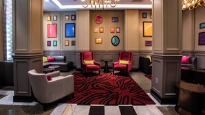 A lobby with a checkered floor, red and black patterned carpet, two red armchairs with yellow cushions, a small round table, and framed artwork on the walls. - Fairfield Inn & Suites by Marriott Philadelphia Downtown/Center City (Philadelphia)