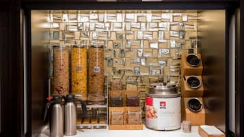 Ein Frühstücksbuffet mit verschiedenen Speisebehältern, einer Kaffeemaschine und einem großen Behälter für Haferflocken.