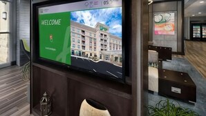 Un espace d’accueil d’hôtel doté d’un grand écran affichant un message de bienvenue et une image du bâtiment.