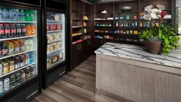 A kitchen area with a marble countertop, a refrigerator stocked with beverages, and shelves with various food items.