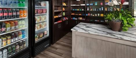 A kitchen area with a marble countertop, a refrigerator stocked with beverages, and shelves with various food items.