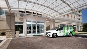 Un bâtiment avec une entrée en verre, un espace de stationnement couvert et un fourgon vert et blanc garé à l’extérieur.