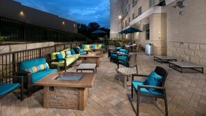 Une terrasse extérieure avec des sièges et des tables, un mur en pierre et un bâtiment en arrière-plan.
