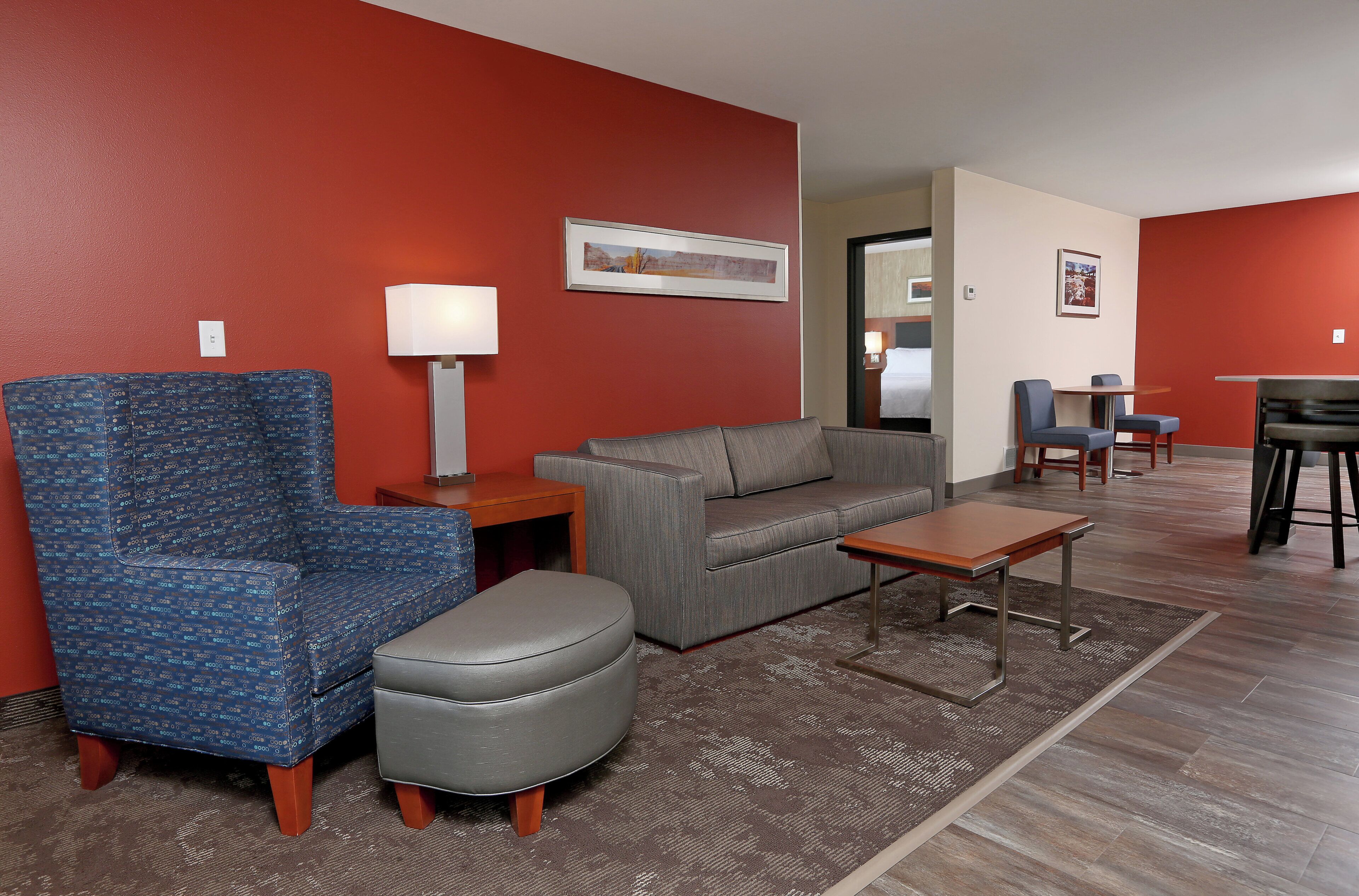 A hotel room with a red wall, a grey sofa, a blue armchair, a small table, and a coffee table.