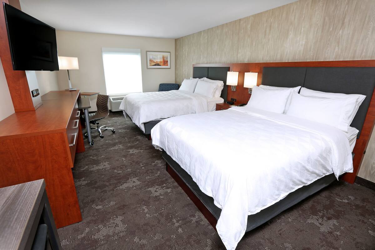 Une chambre d’hôtel avec deux lits, un bureau, un téléviseur à écran plat et une fenêtre.