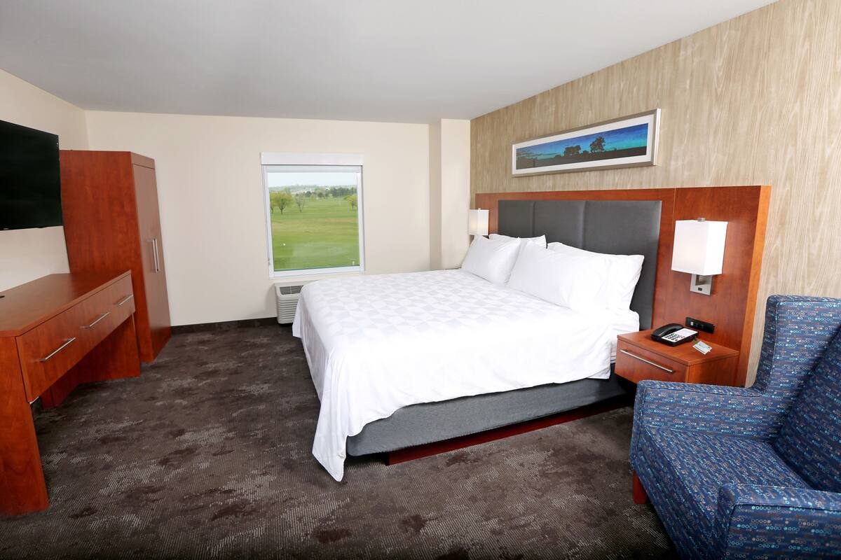 Une chambre d’hôtel comprenant un lit, un bureau, une chaise, un téléviseur, une fenêtre donnant sur un terrain de golf et un tableau accroché au mur.