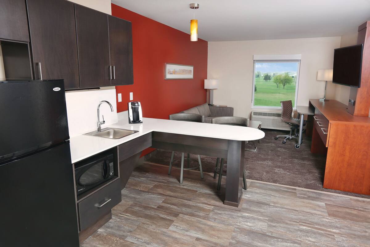 Une cuisine moderne avec des meubles de couleur sombre, un plan de travail blanc et un four à micro-ondes encastré.