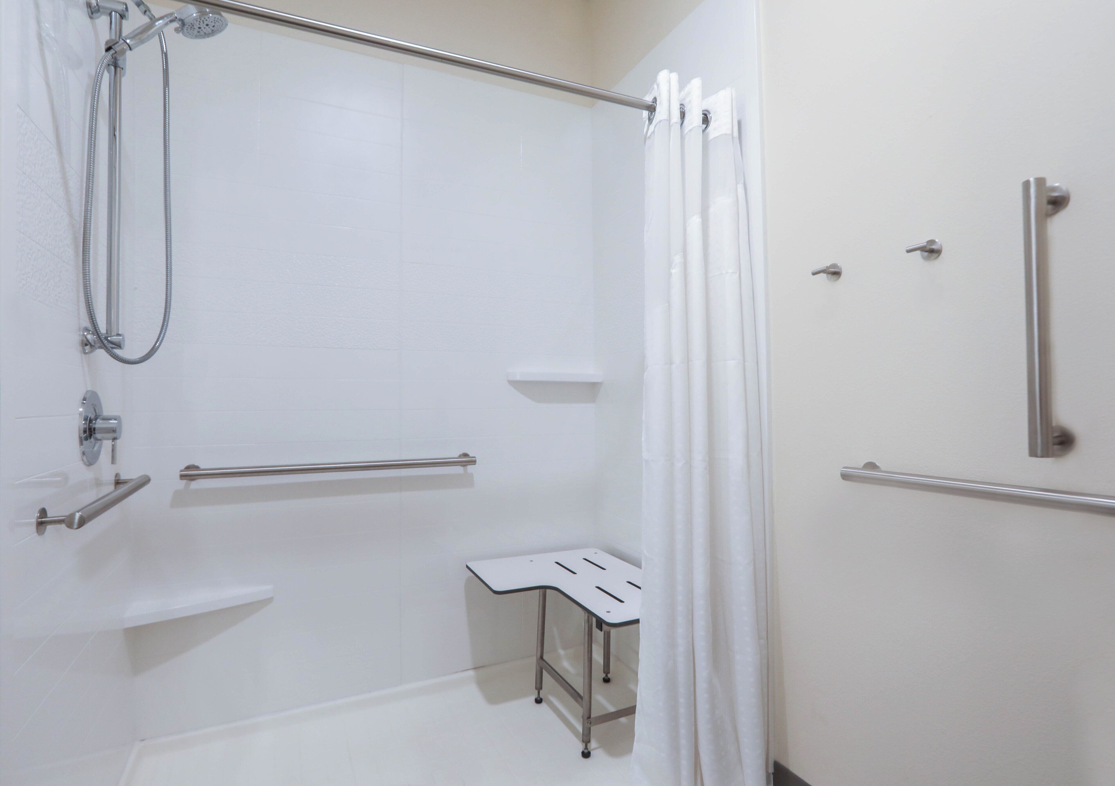 Ein helles Badezimmer mit Dusche, Haltegriffen und einer kleinen weißen Sitzbank.