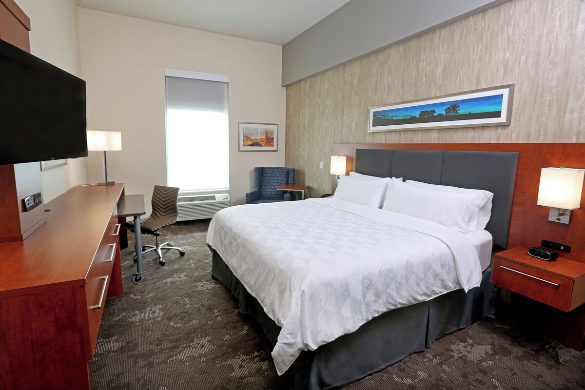 Une chambre d’hôtel équipée d’un lit, d’un bureau, d’une chaise, d’une télévision et d’œuvres d’art accrochées au mur.