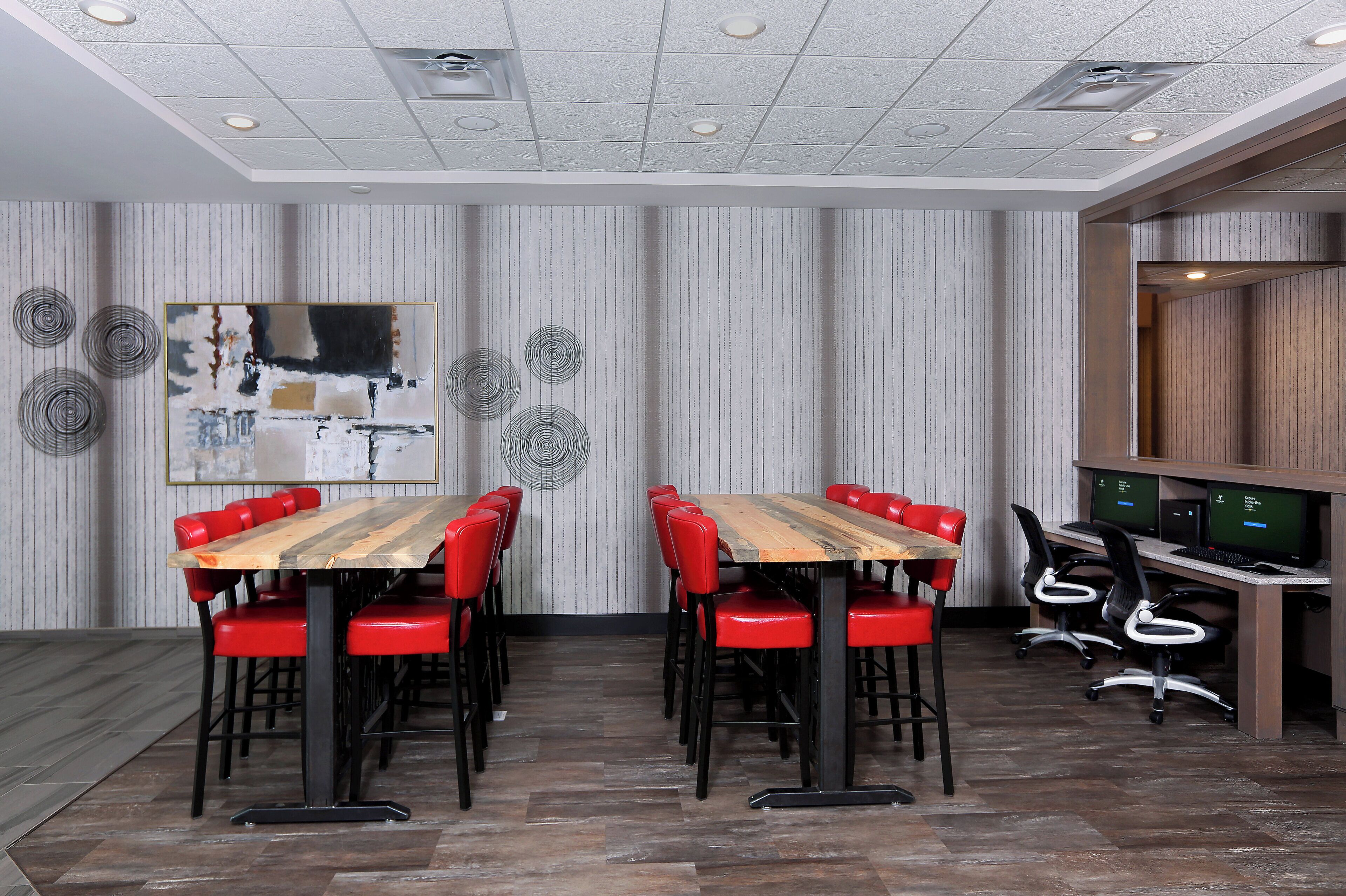 A conference room with a long table, red chairs, a painting on the wall, and a computer station.